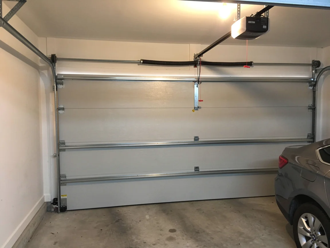 A white garage door is closed with an opener and a car parked inside.